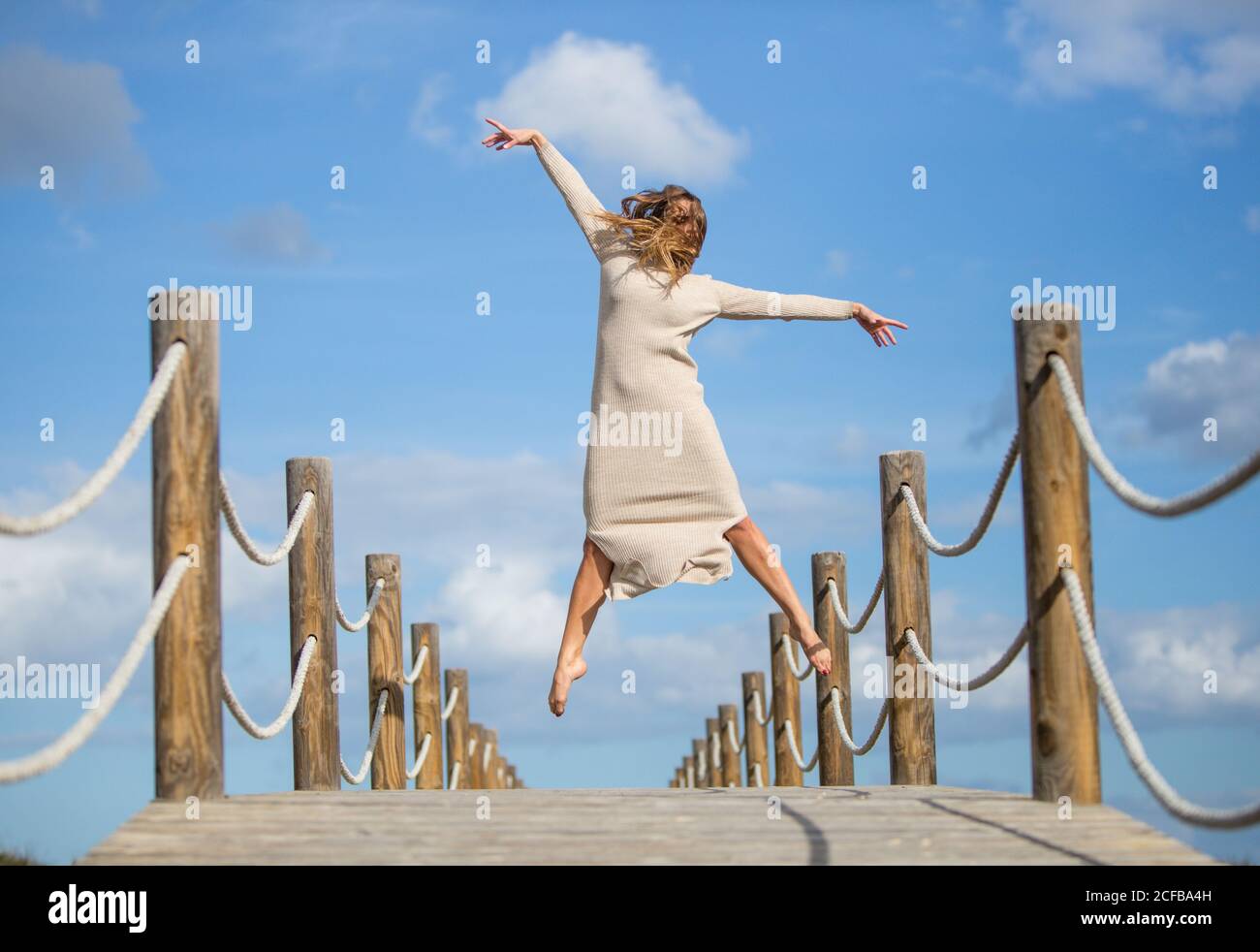 Vue arrière de la jeune ballerine en gris avec du blanc textile dans l'air sur la passerelle et ciel bleu ensoleillé jour Banque D'Images