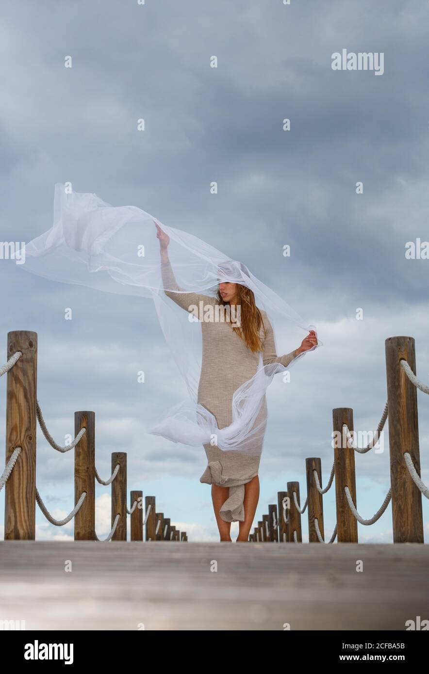 Vue arrière de la jeune ballerine en gris avec du blanc textile dans l'air sur la passerelle et ciel bleu ensoleillé jour Banque D'Images