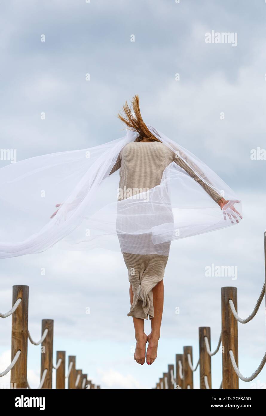 Vue arrière de la jeune ballerine en gris avec du blanc textile dans l'air sur la passerelle et ciel bleu ensoleillé jour Banque D'Images