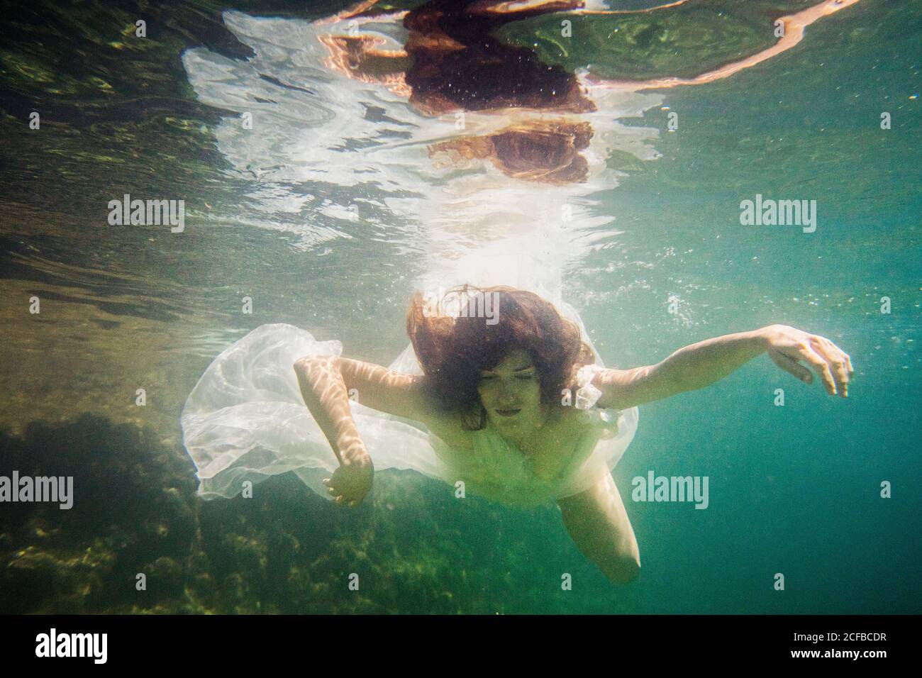 Une femme nue danse et plonge avec des tissus transparents sous la mer Banque D'Images