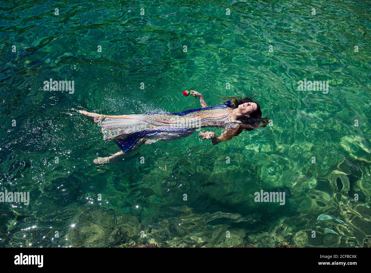 Une femme flotte dans la mer avec une rose dans sa main, prétendant être noyée Banque D'Images