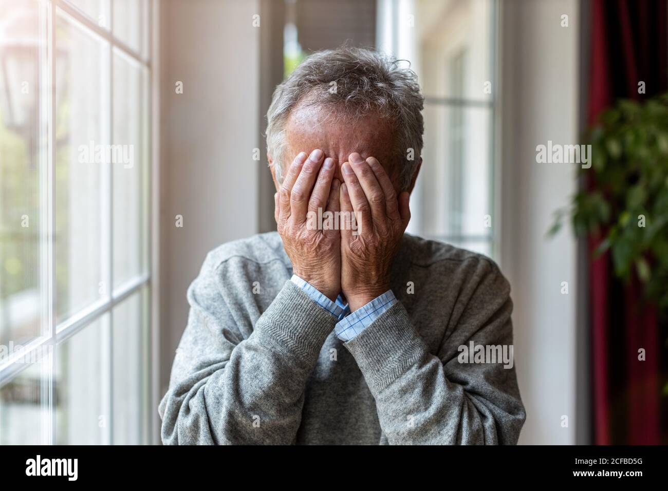 Homme âgé tenant la tête entre les mains dans le désespoir Banque D'Images