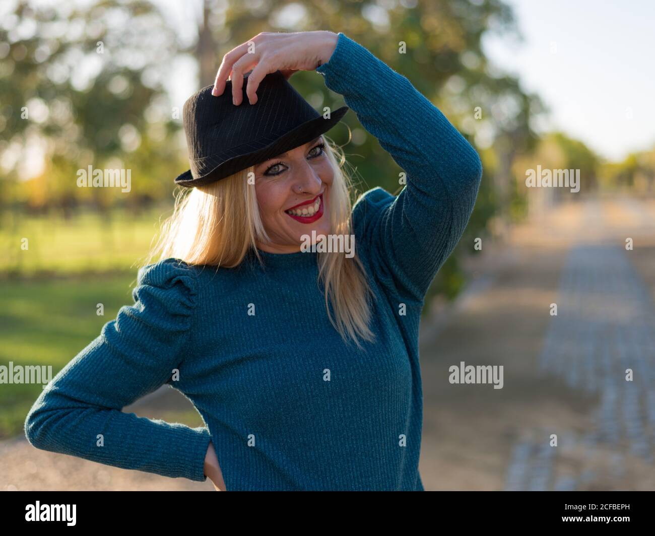 Jeune femme blonde en chapeau. Regarder l'appareil photo et sourire heureux. Une journée ensoleillée à l'extérieur. Banque D'Images