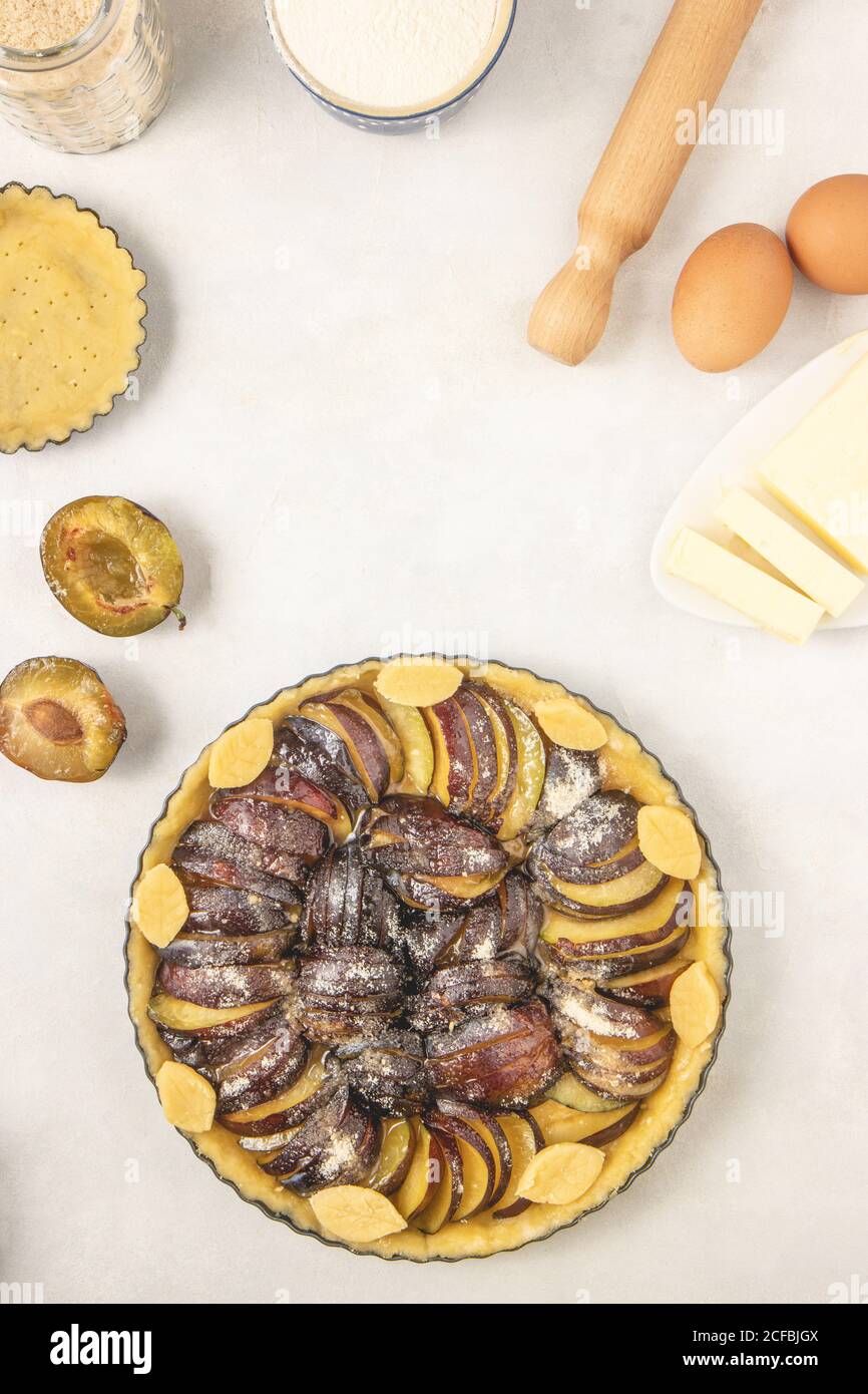 Tarte maison avec prunes et sucre sur fond blanc. Faire démarrer avec des prunes brutes. Vue de dessus, plan d'appartement. Banque D'Images