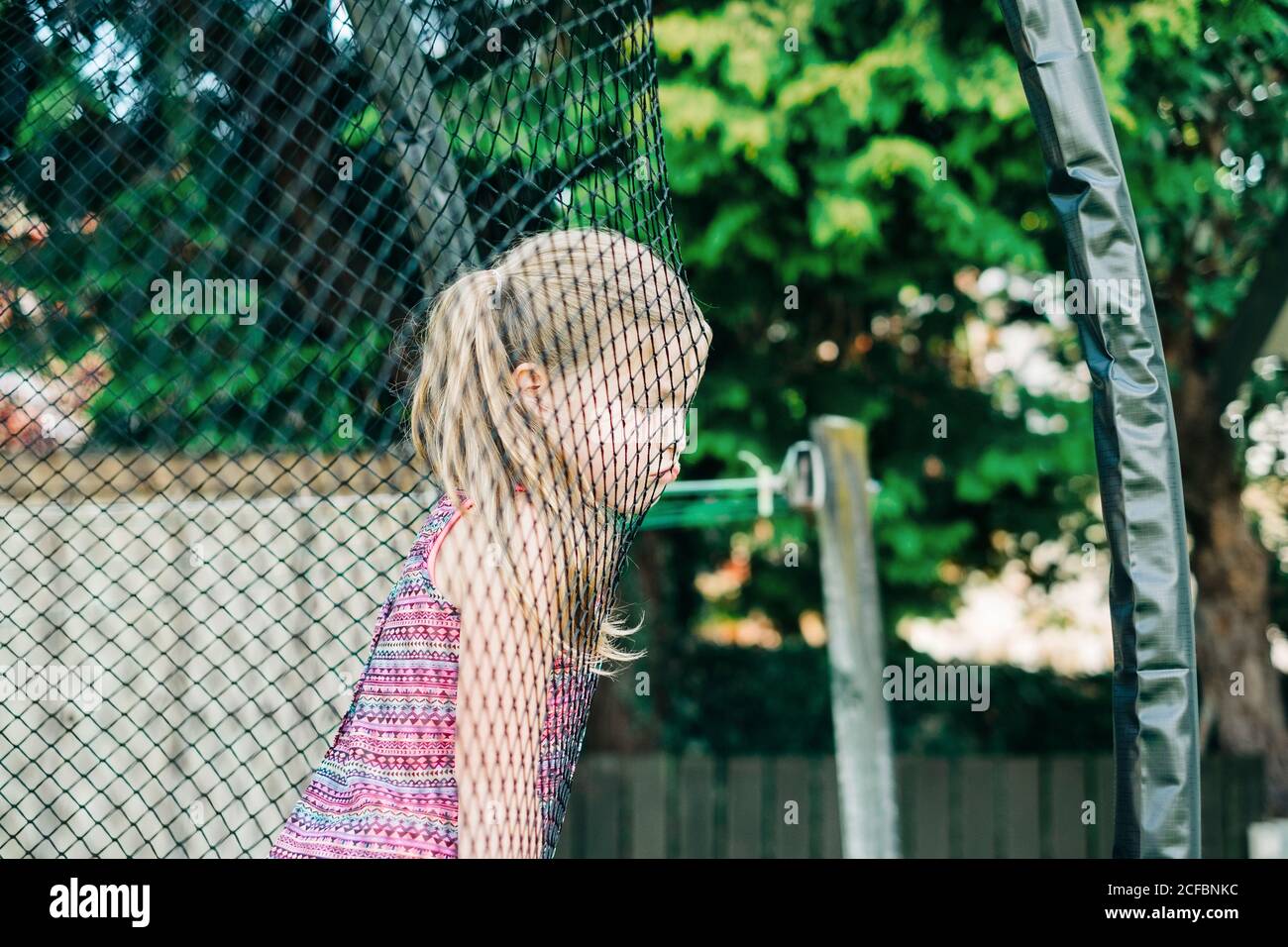 Jeune fille au visage grincheux penchée sur un filet de trampoline Banque D'Images