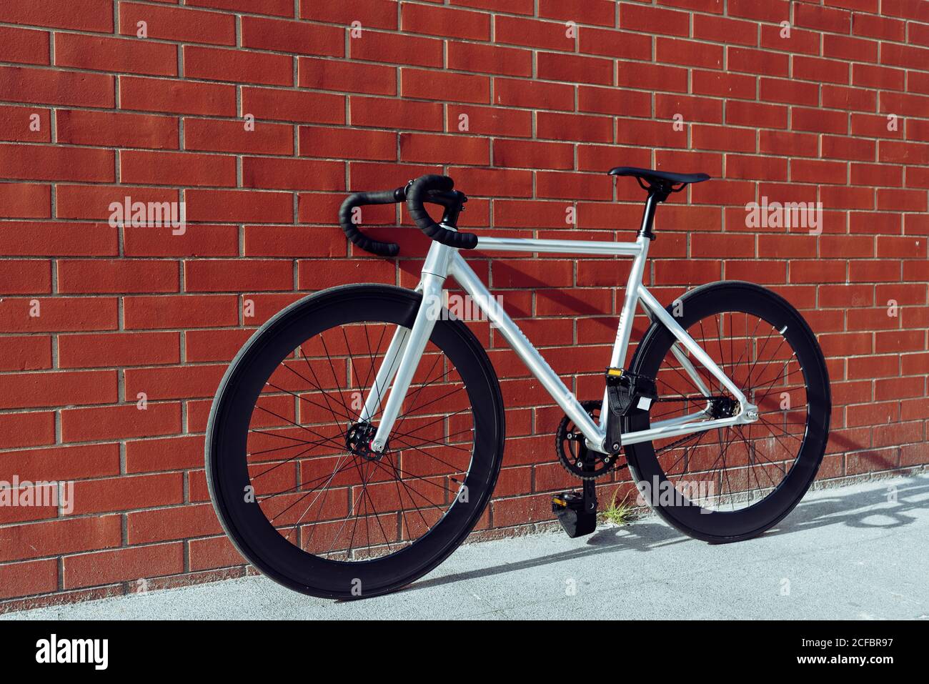 Nouveau vélo de route blanc moderne avec barre de poignée noire garée contre le mur de briques rouges Banque D'Images