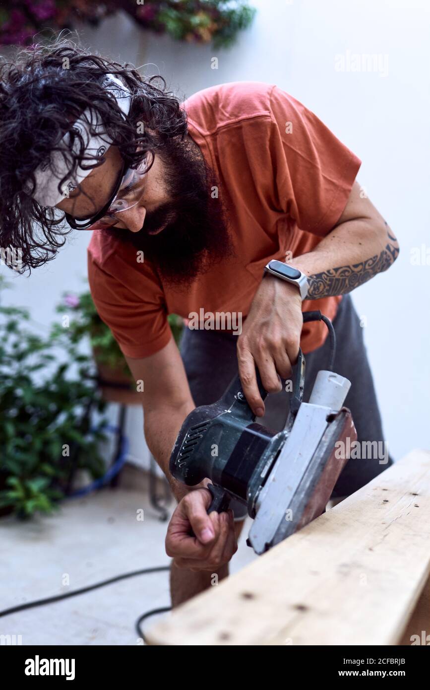 Jeune homme barbe polissage d'une planche en bois avec une ponceuse électrique. Concept du travail des femmes Banque D'Images