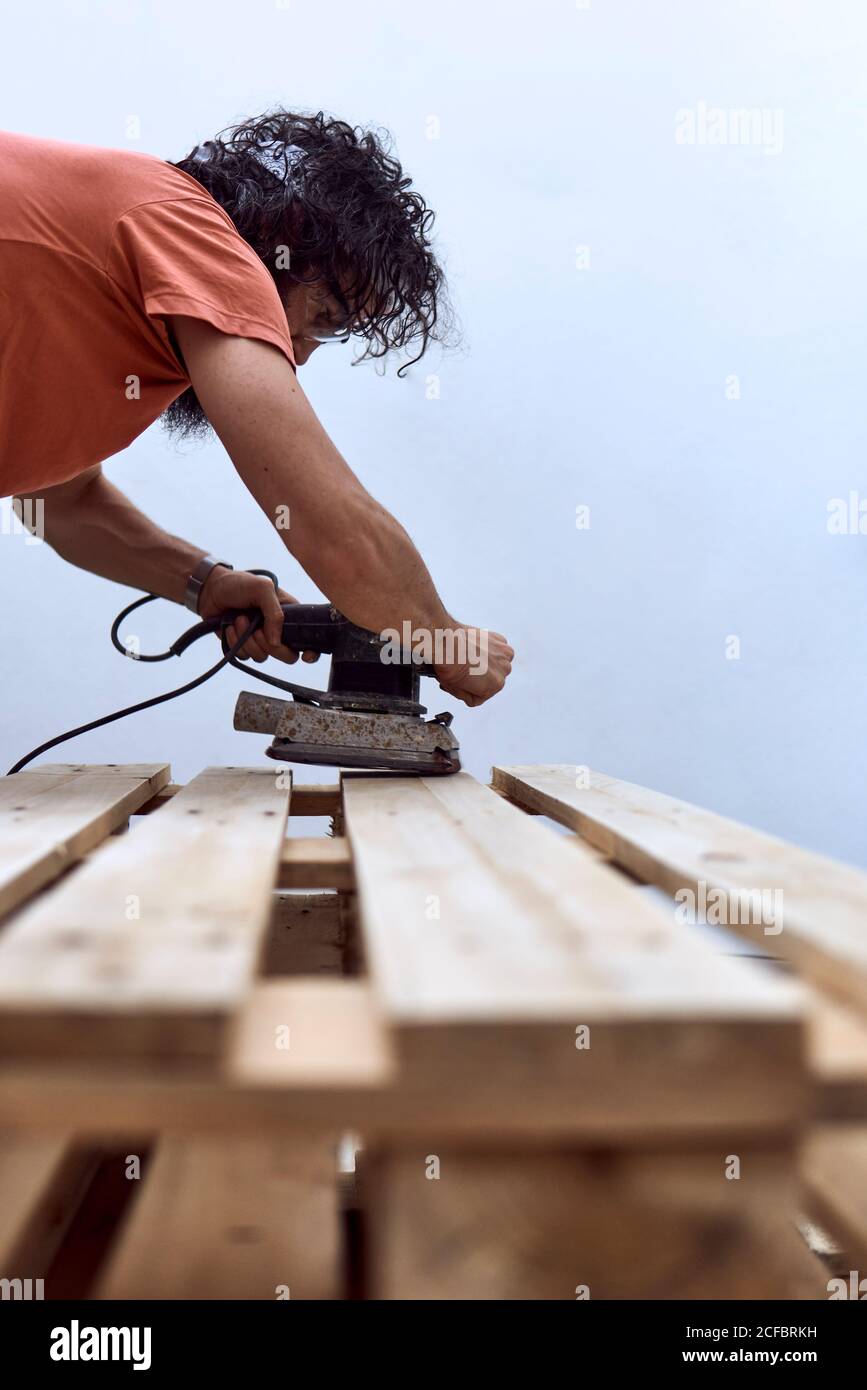 Jeune homme barbe polissage d'une planche en bois avec une ponceuse électrique. Concept du travail des femmes Banque D'Images