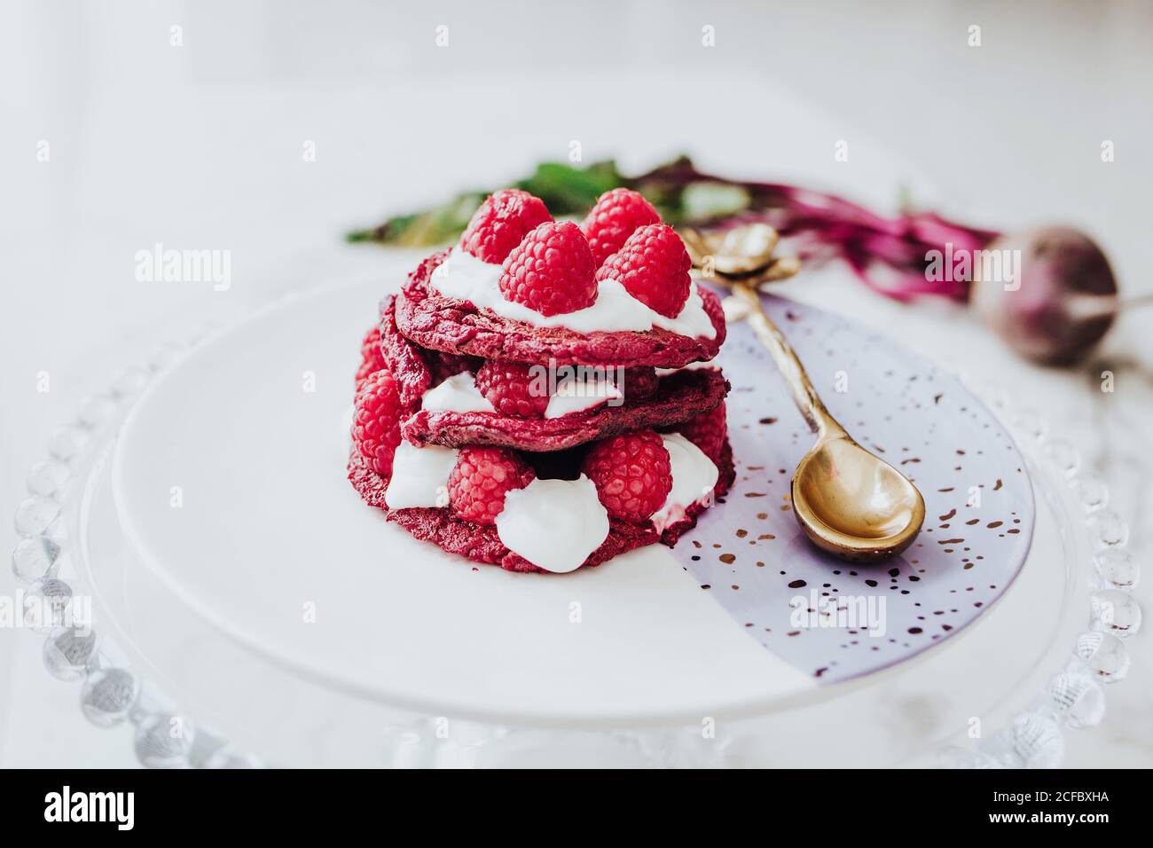 De délicieuses crêpes de betteraves biologiques à la framboise fraîche sur l'assiette avec une cuillère dorée sur une table blanche Banque D'Images