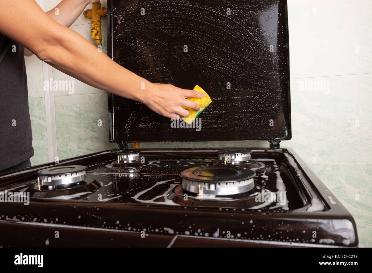 nettoyage de la cuisine, nettoyage de surface sur la cuisinière à gaz, lavage de la cuisinière avec un linge de toilette jaune, appareils ménagers de cuisine. Banque D'Images