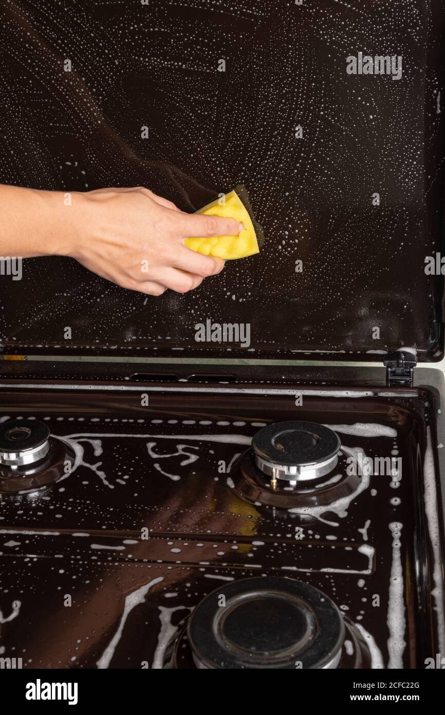 nettoyage de la cuisine, nettoyage de surface sur la cuisinière à gaz, lavage de la cuisinière avec un linge de toilette jaune, appareils ménagers de cuisine. Banque D'Images