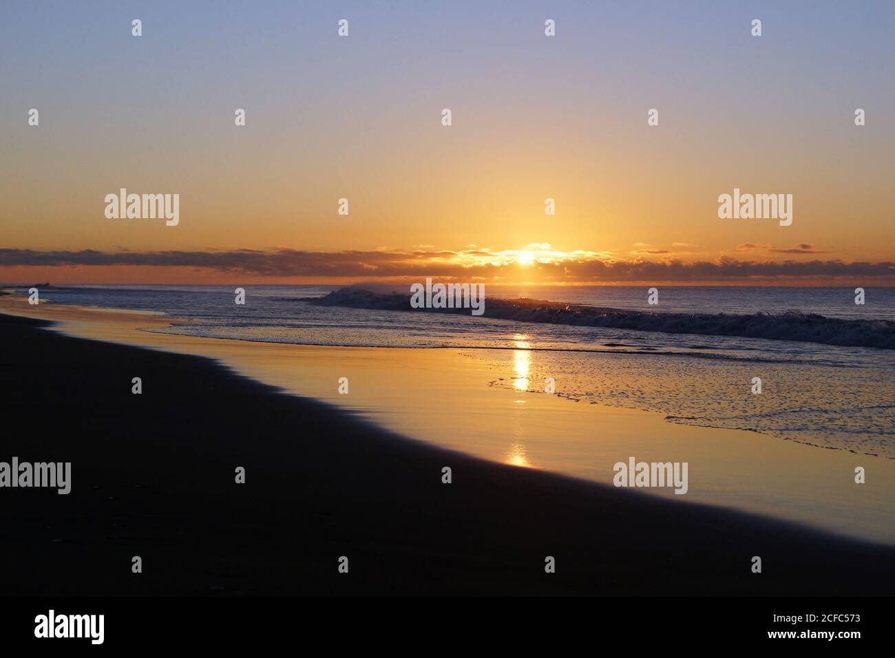 Coucher de soleil vibrant dans un ciel très nuageux sur une plage ondulée tranquille avec plage de sable Banque D'Images