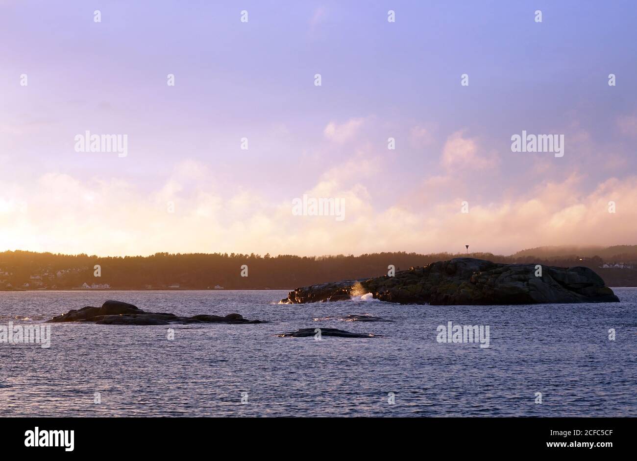 Rochers gris au bord de la mer paisible lors d'une journée froide et brumeuse avec ciel clair et coloré Banque D'Images