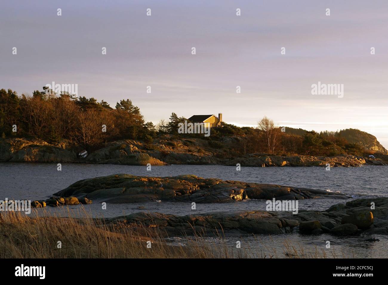 Rochers gris et maison au bord de la mer paisible sur la brumeuse fraîche journée au ciel clair et coloré Banque D'Images