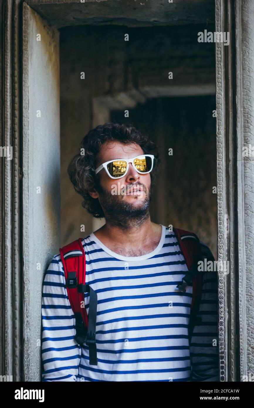 Homme barbu adulte en lunettes de soleil et avec sac à dos debout dans le cadre de porte en pierre, Thaïlande Banque D'Images