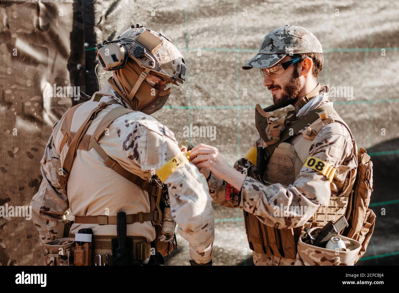 Homme barbu en camouflage attachant la bande d'identification du bras de escadron tout en se préparant à jouer à la partie airsoft ensemble Banque D'Images