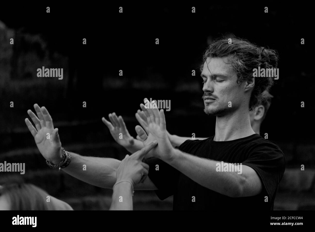 Homme tranquille étirant les mains et pratiquant la méditation qigong avec la récolte partenaire touchant les paumes avec les doigts Banque D'Images