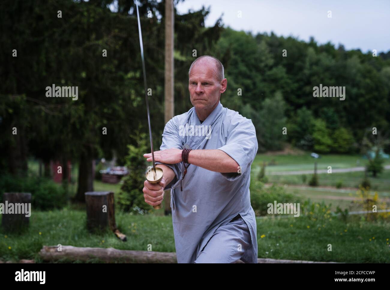 Déterminé homme d'âge moyen dans kimono se concentrant et en utilisant l'épée tout en s'entraîner seul dans le jardin Banque D'Images