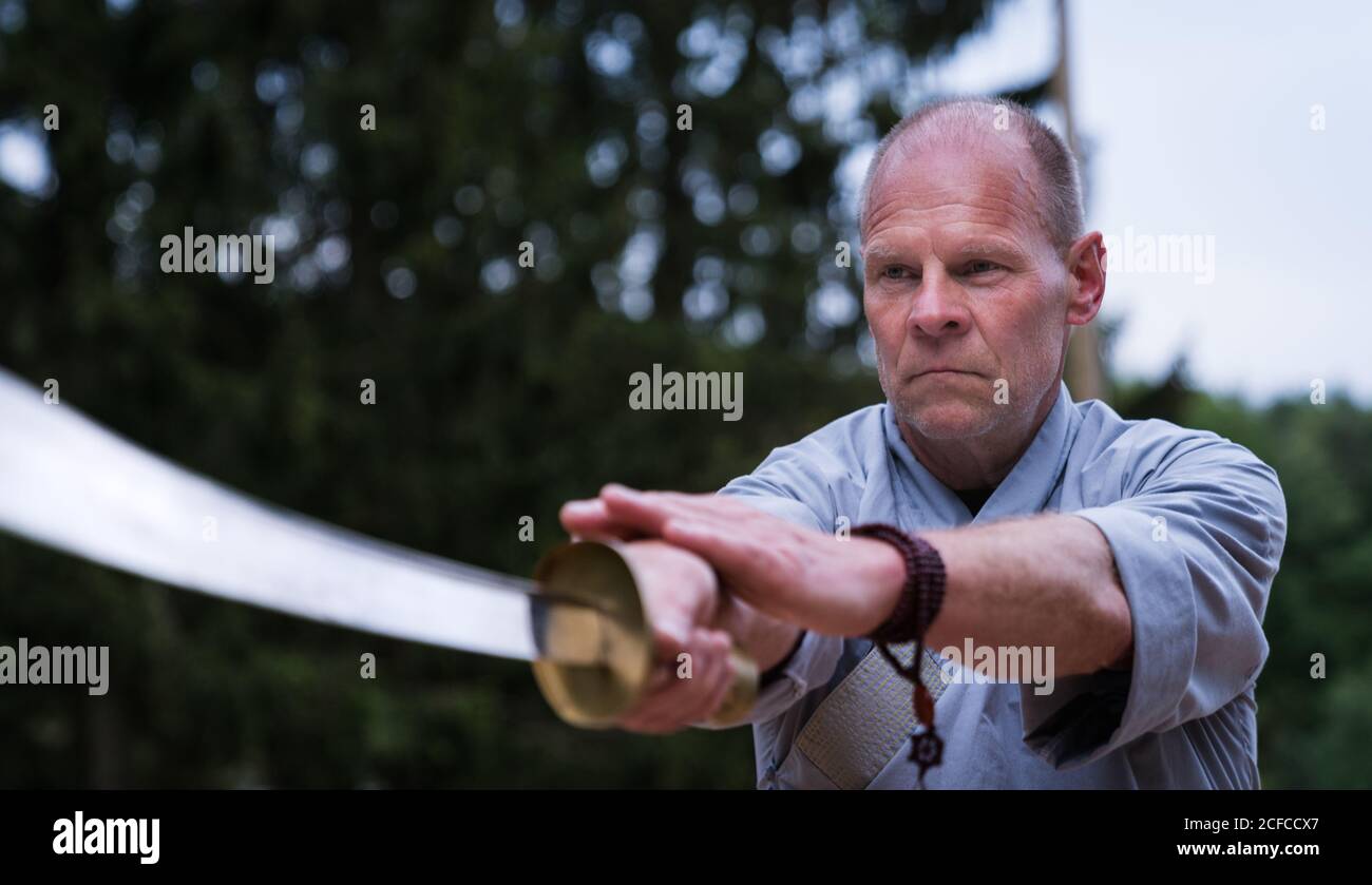 Déterminé homme d'âge moyen dans kimono se concentrant et en utilisant l'épée tout en s'entraîner seul dans le jardin Banque D'Images