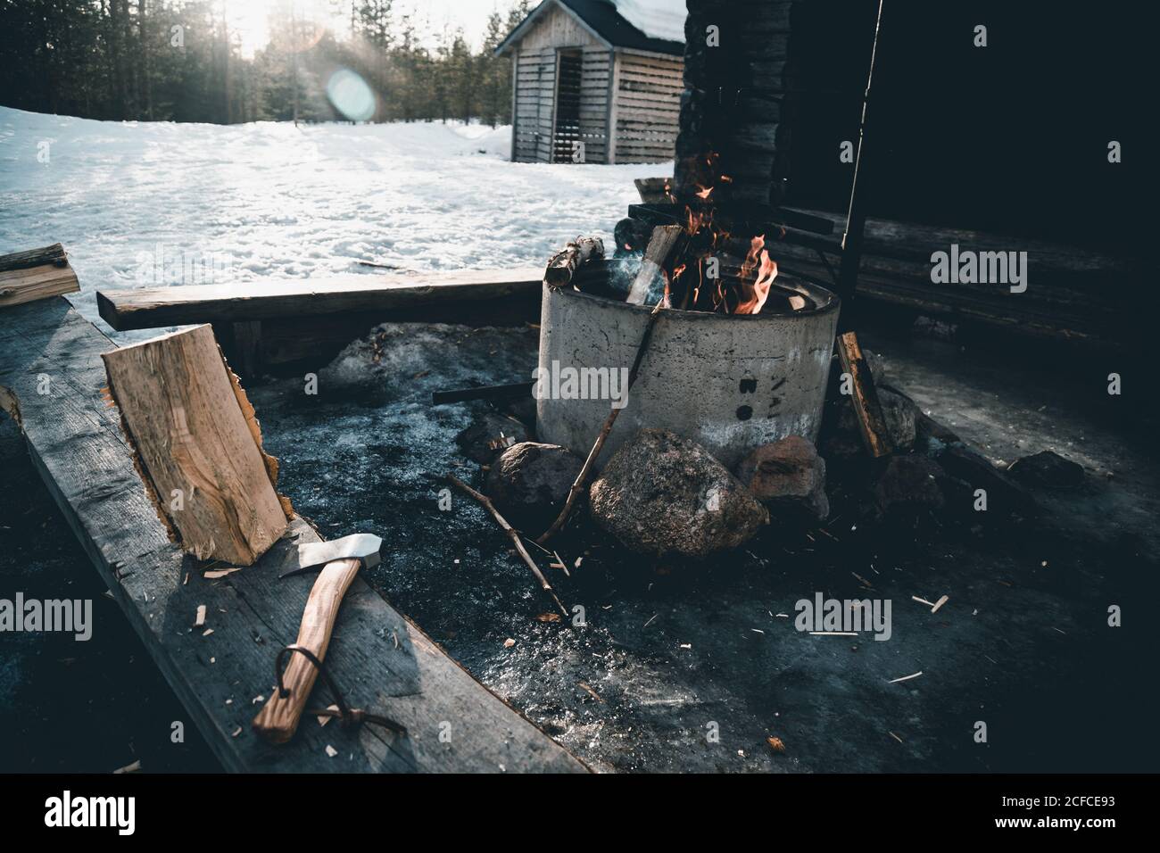 Feu de camp et feu de bois avec hache placé près de la petite cabine de bûcherons dans la forêt enneigée en hiver dans la campagne De Finlande Banque D'Images