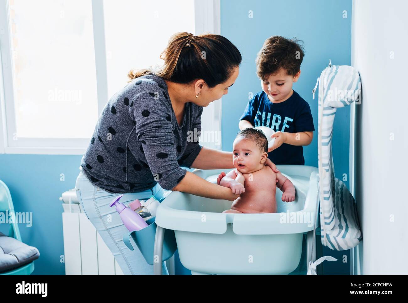 Femme De Soin Adulte En Lavant Doucement Bebe Dans Le Bain De Bebe Dans La Salle De Bains Confortable Pendant Que Le Petit Fils Aide Maman Et De Tenir Bol D Eau Chaude