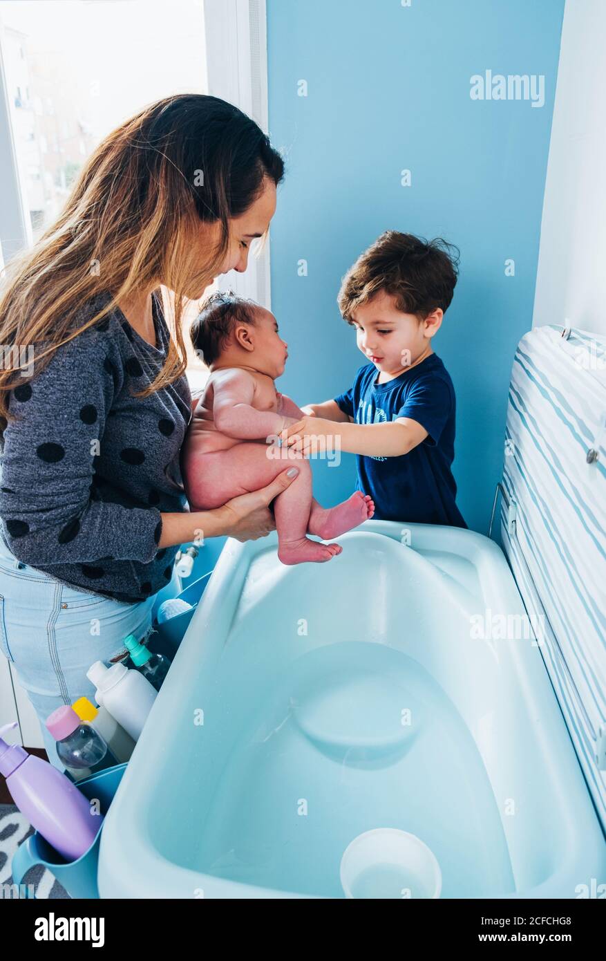 Femme De Soin Adulte En Lavant Doucement Bebe Dans Le Bain De Bebe Dans La Salle De Bains Confortable Pendant Que Le Petit Fils Aide Maman Et De Tenir Bol D Eau Chaude