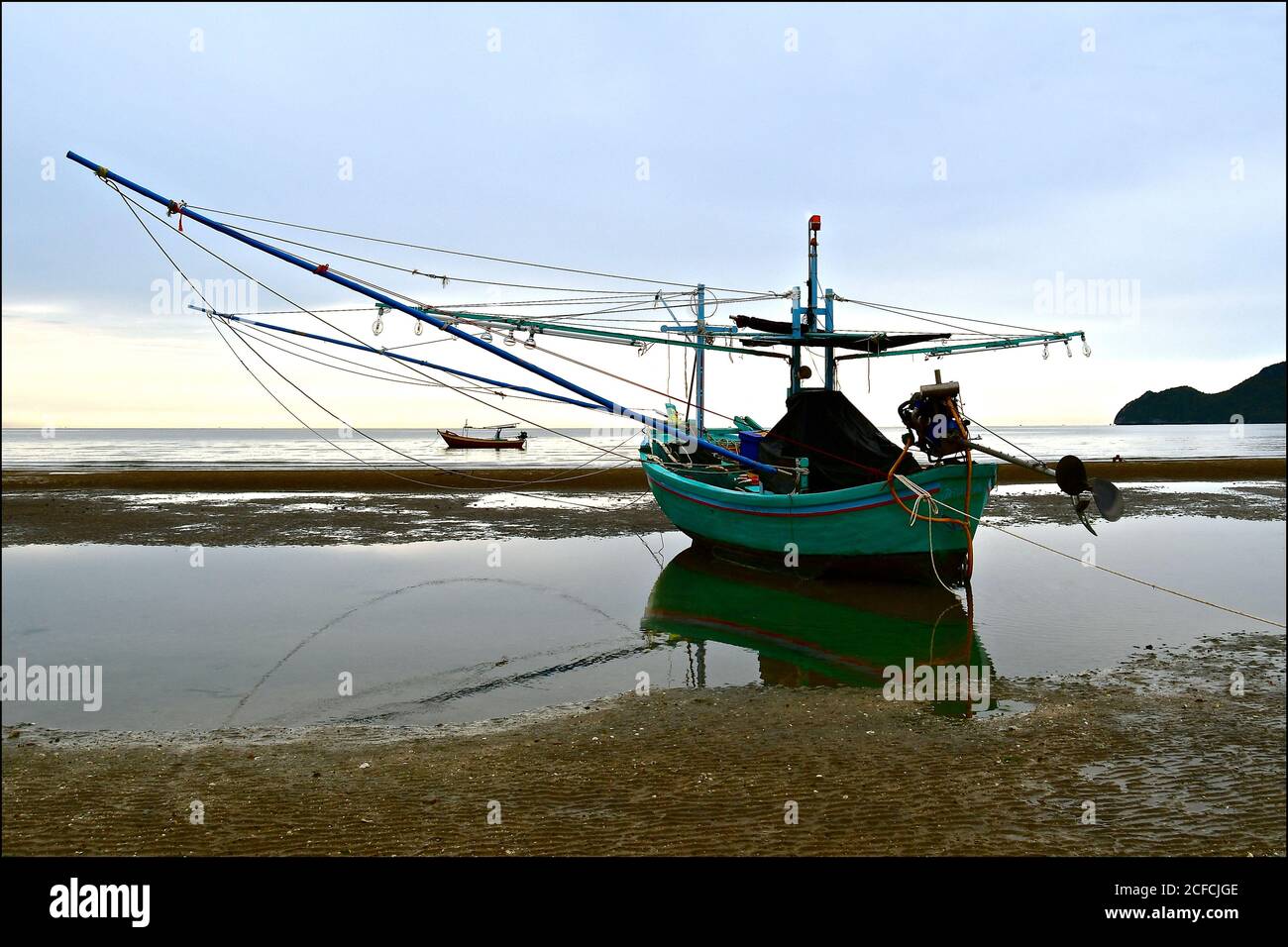 Un bateau de pêche asiatique traditionnel en bois avec grillage amarré à marée basse, il y a un miroir dans l'eau calme. Banque D'Images