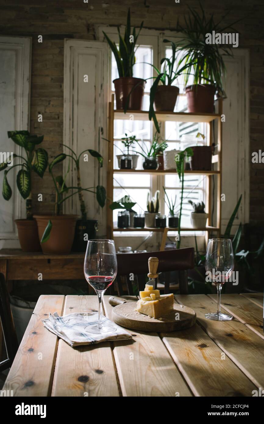 Verres avec vin rouge placés près du fromage sur une table en bois dans un restaurant rustique avec plantes vertes en pot sur la fenêtre Banque D'Images