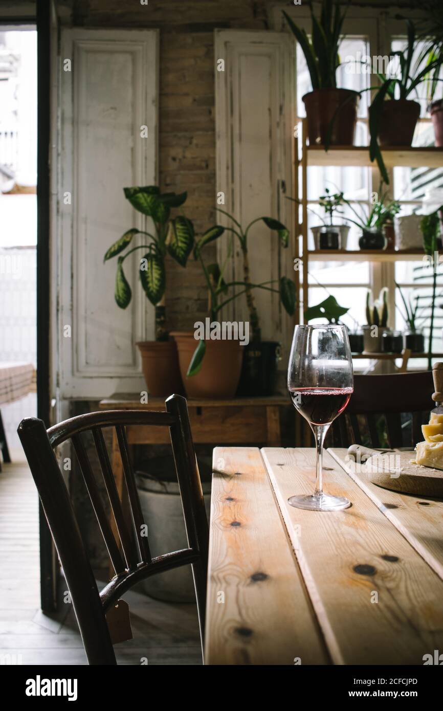 Verres avec vin rouge placés près du fromage sur une table en bois dans un restaurant rustique avec plantes vertes en pot sur la fenêtre Banque D'Images