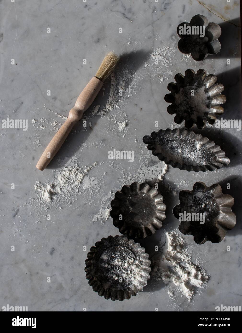 Vue de dessus de divers moules à pâtisserie en métal et petite cuisine badigeonner sur une table en marbre parsemée de farine blanche Banque D'Images