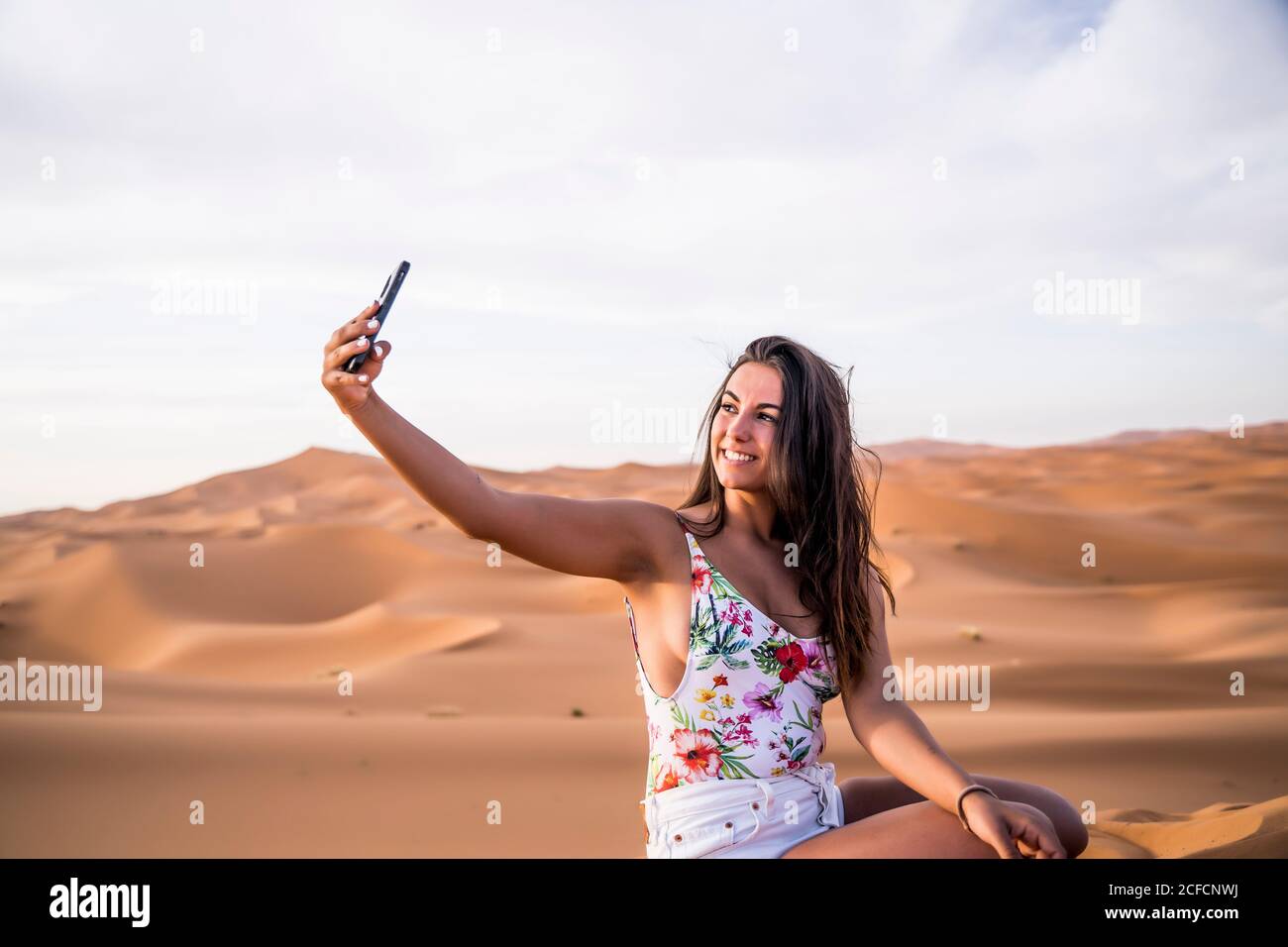 Jeune femme prenant selfie avec téléphone au milieu du désert sablonneux, au Maroc Banque D'Images