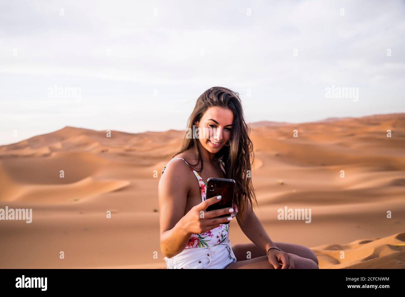Jeune femme prenant selfie avec téléphone au milieu du désert sablonneux, au Maroc Banque D'Images
