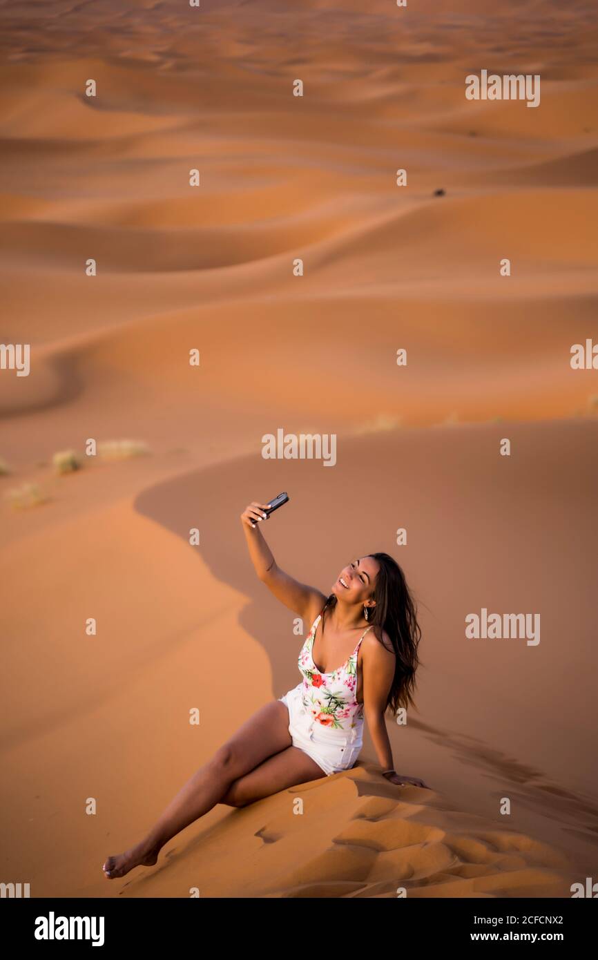 Jeune femme prenant selfie avec téléphone au milieu du désert sablonneux, au Maroc Banque D'Images