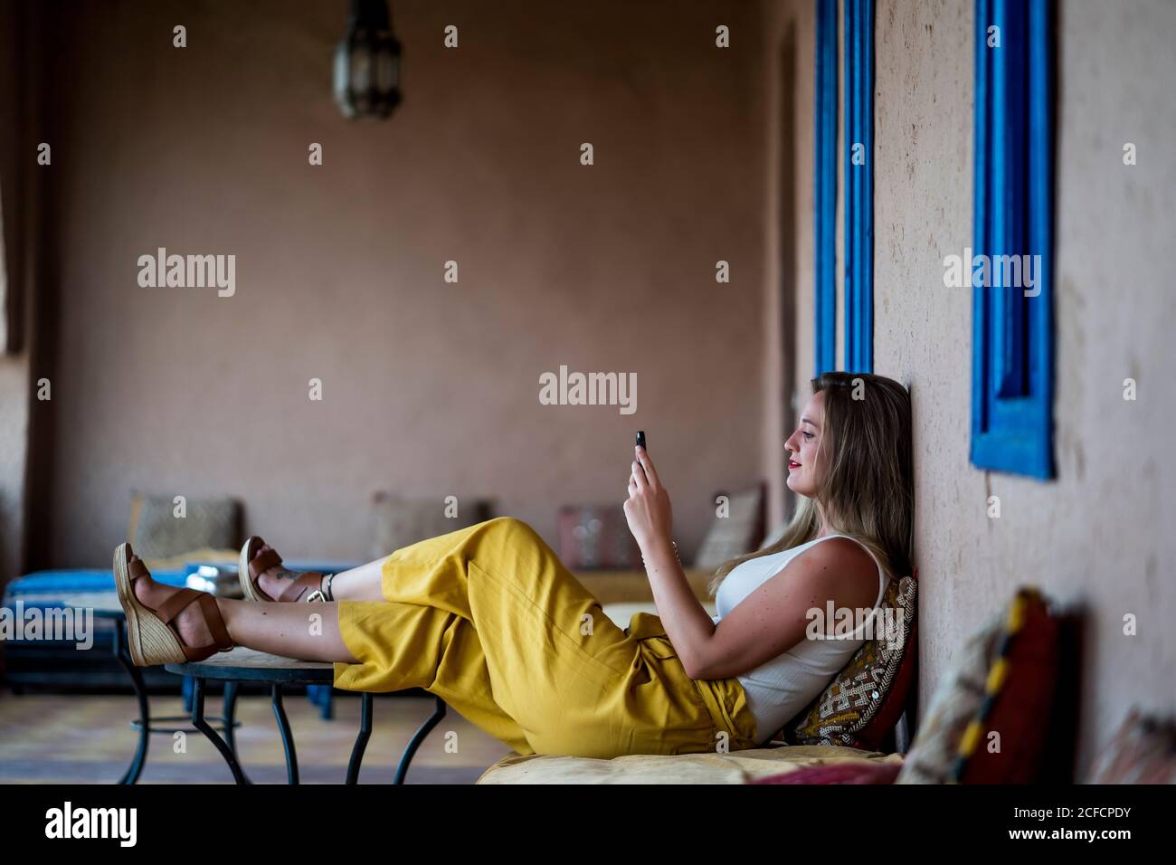 Femme adulte assise sur un canapé en terrasse de style oriental et utilisant un téléphone portable au Maroc Banque D'Images