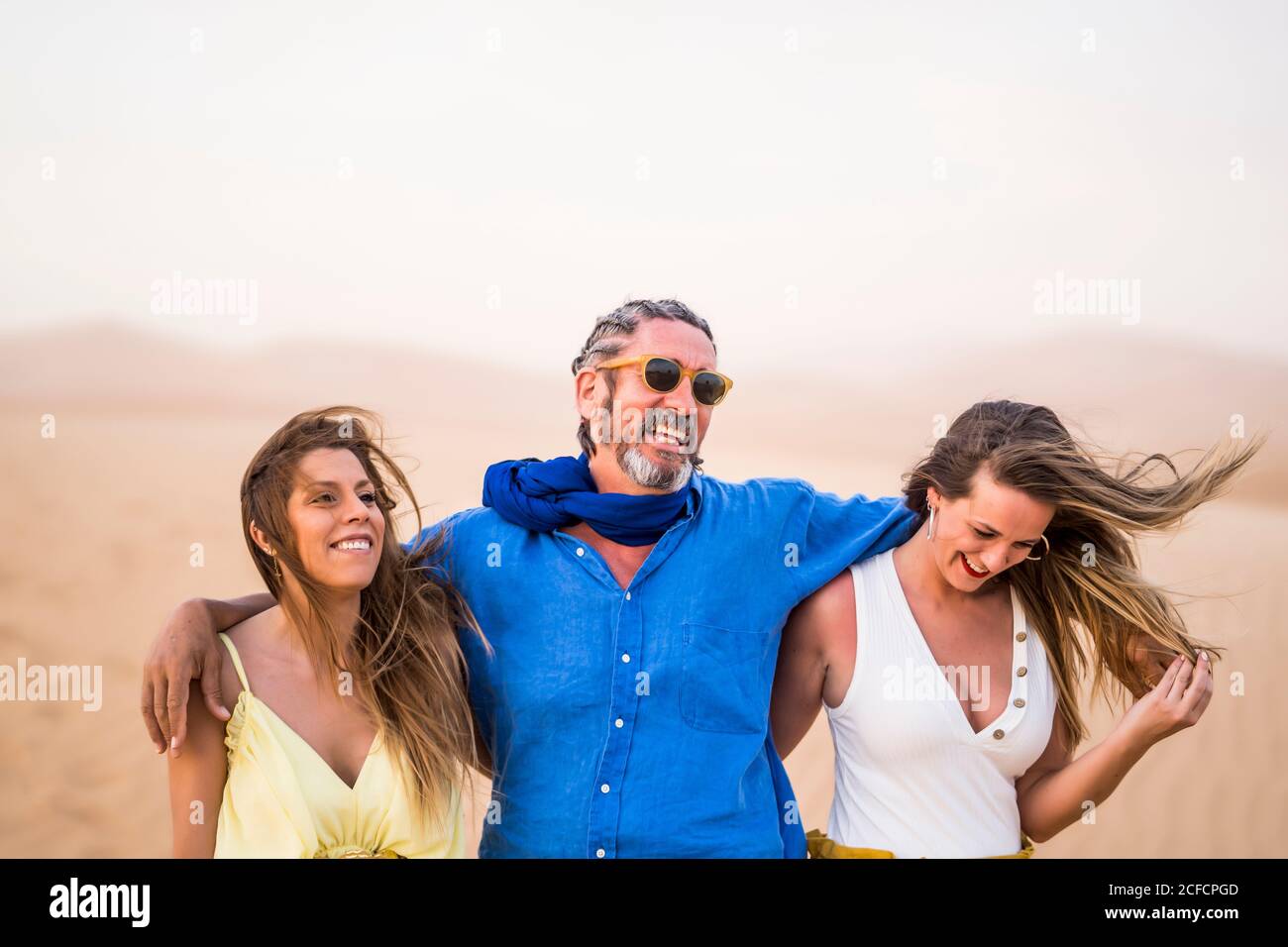 Homme barbu senior riant et embrassant les femmes gaies en marchant Dans le désert de sable pendant le voyage au Maroc Banque D'Images