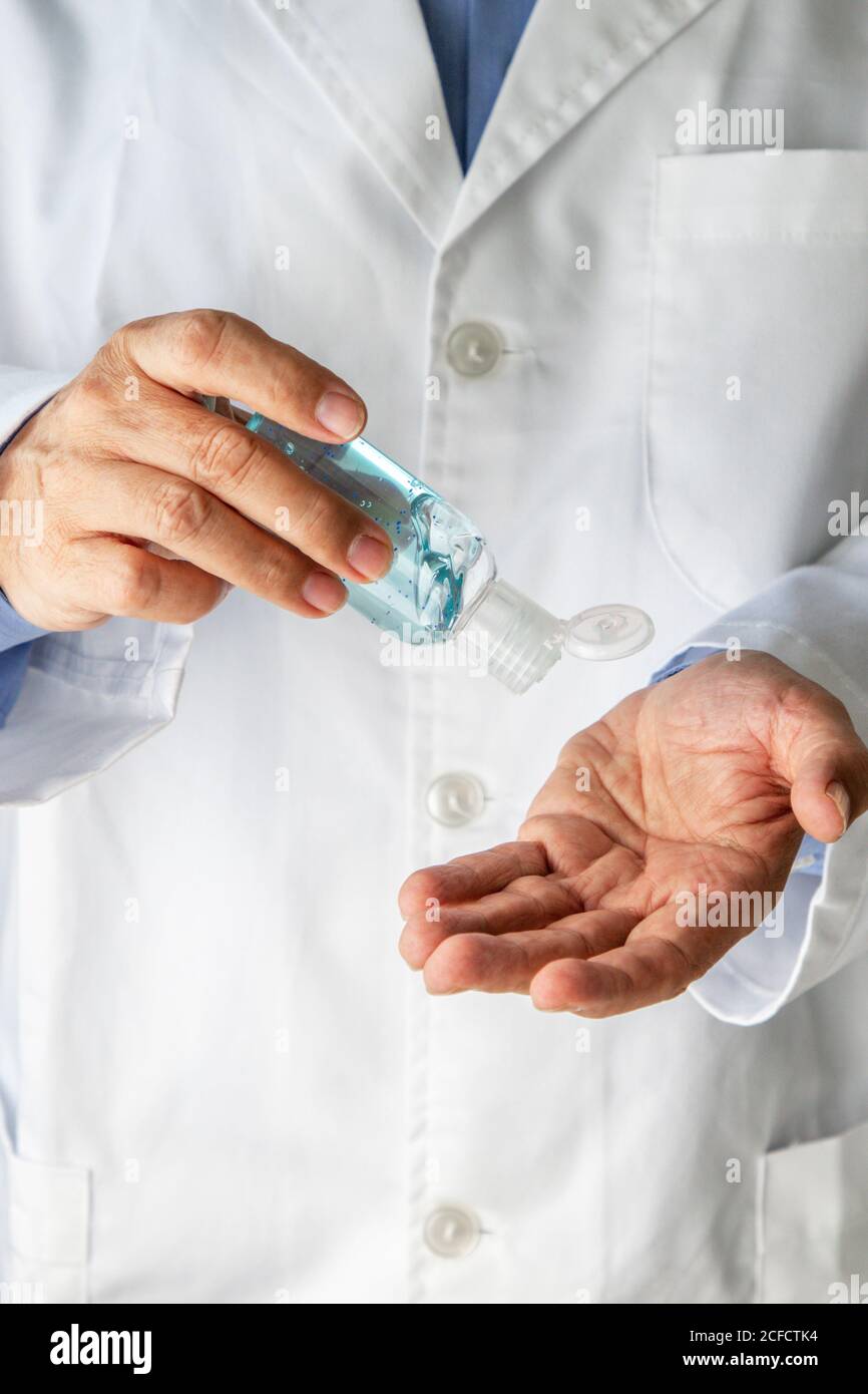 Crop homme médecin généraliste en robe médicale appliquant le gel antibactérien pour la désinfection des mains sur fond gris dans clinique pendant une pandémie de coronavirus Banque D'Images