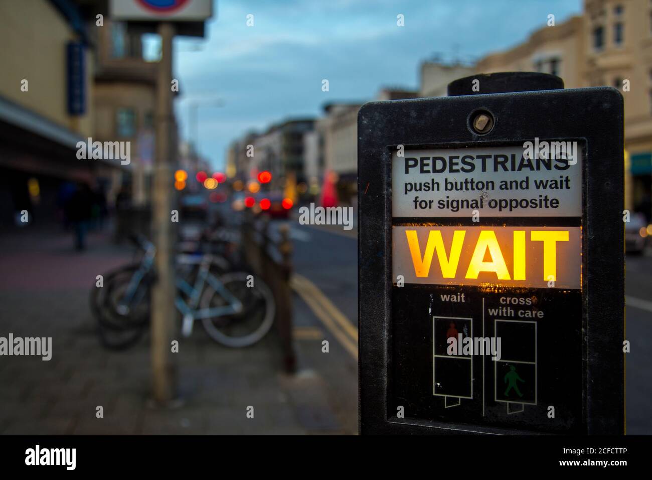 Panneau d'instructions moderne pour les feux de circulation avec signal d'attente lumineux sur fond flou de rue du soir à Brighton, Angleterre Banque D'Images