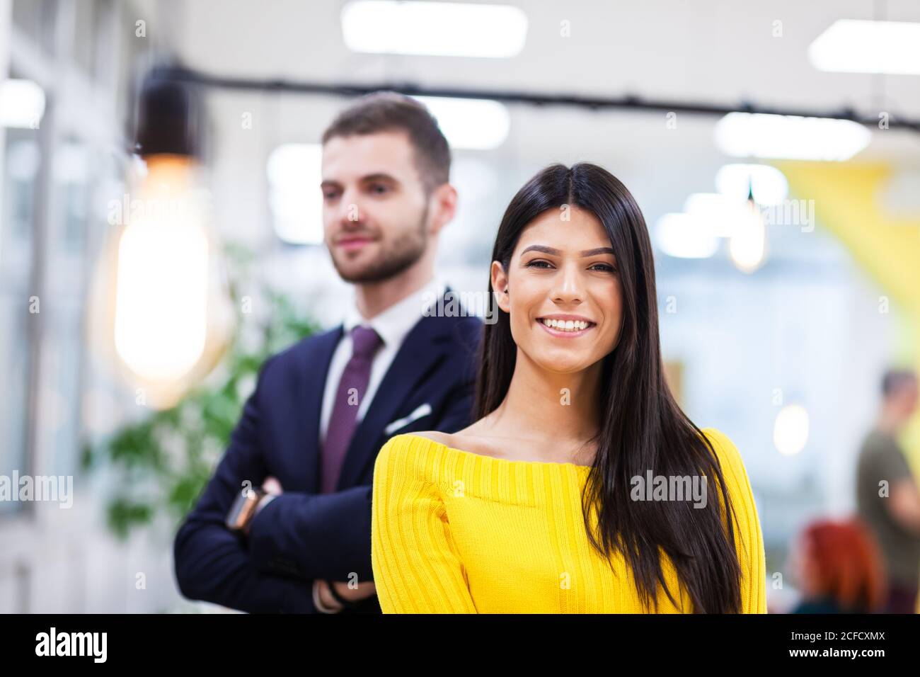 Belle fille caucasienne à cheveux foncés en jaune posant avec homme d'affaires portant le costume. Des collègues heureux dans un bureau moderne Banque D'Images