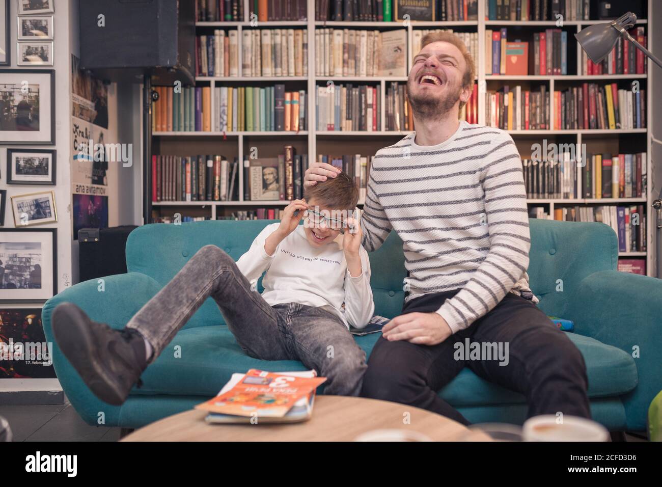 Père et fils s'amusent tout en étant assis sur un canapé séjour avec livres Banque D'Images