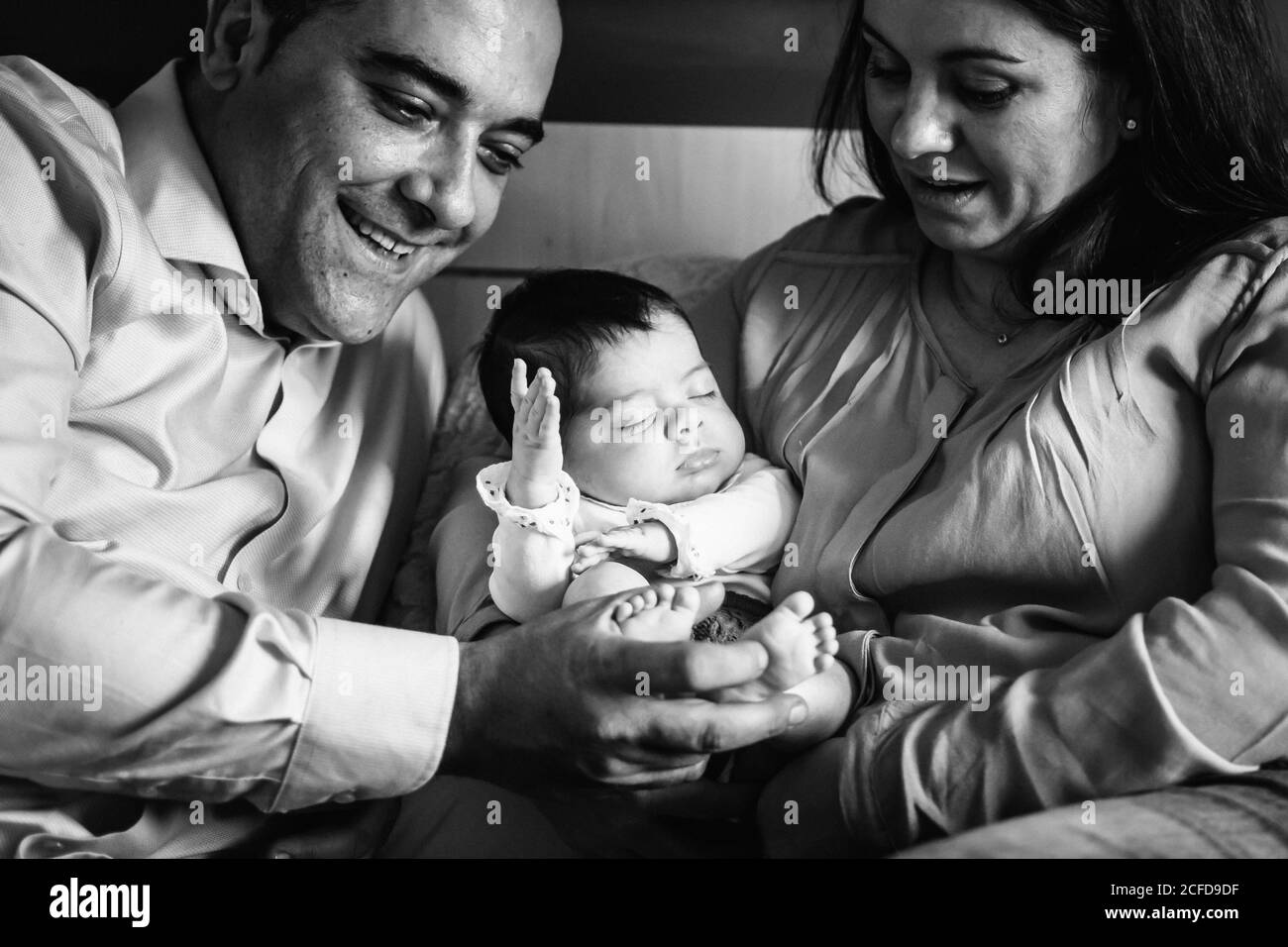 Père souriant tenant rire petite fille couché sur le lit avec mère tenant bébé nouveau-né Banque D'Images