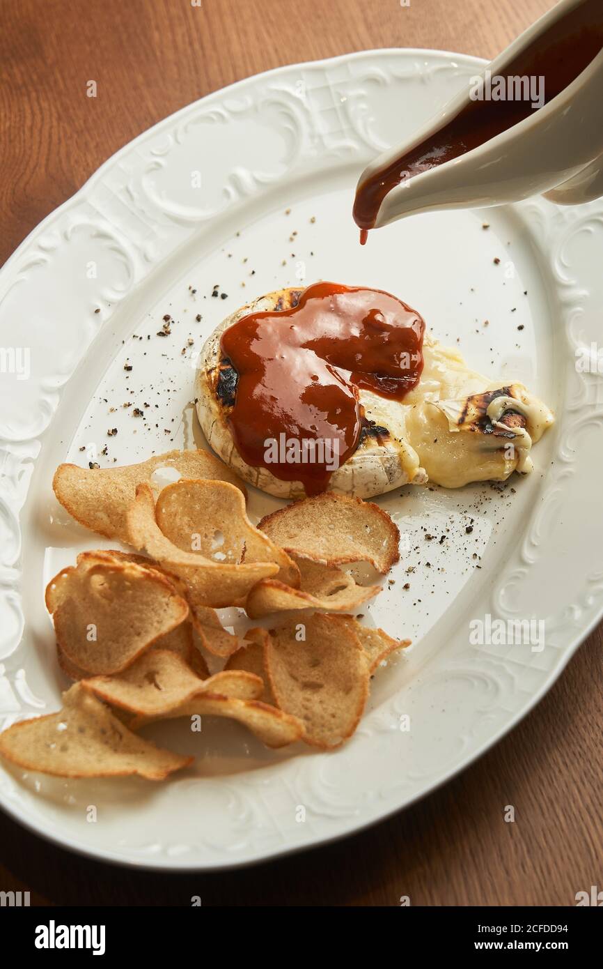 Par le dessus, personne méconnaissable verse de la sauce barbecue sur de délicieux grillades fromage à la crème et chips de pain sur l'assiette de la table Banque D'Images