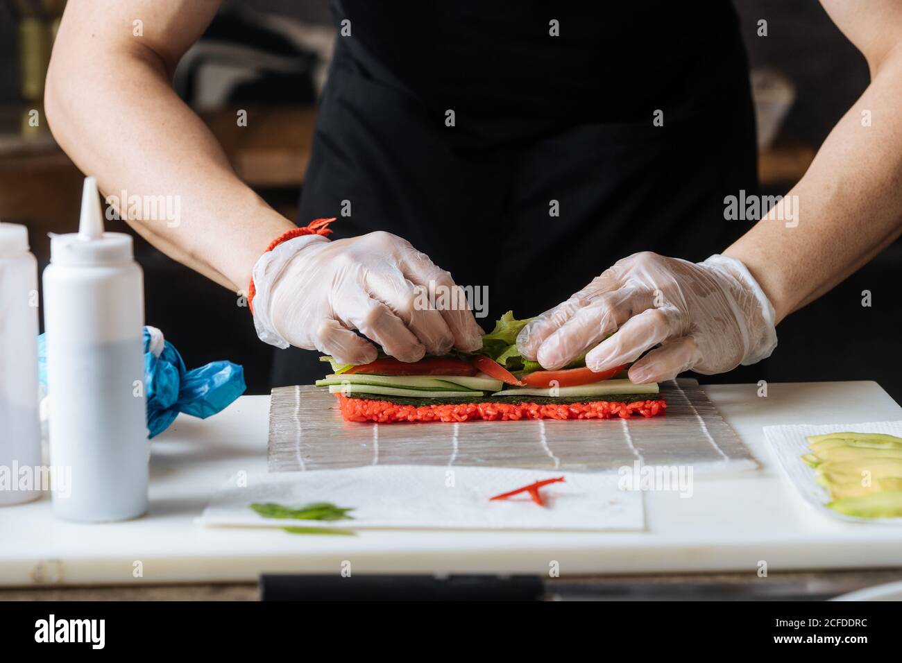 Préparation culinaire en gants jetables pétrissant la farce épicée rouge sur une table avec du poisson vert et des sauces dans la cuisine Banque D'Images