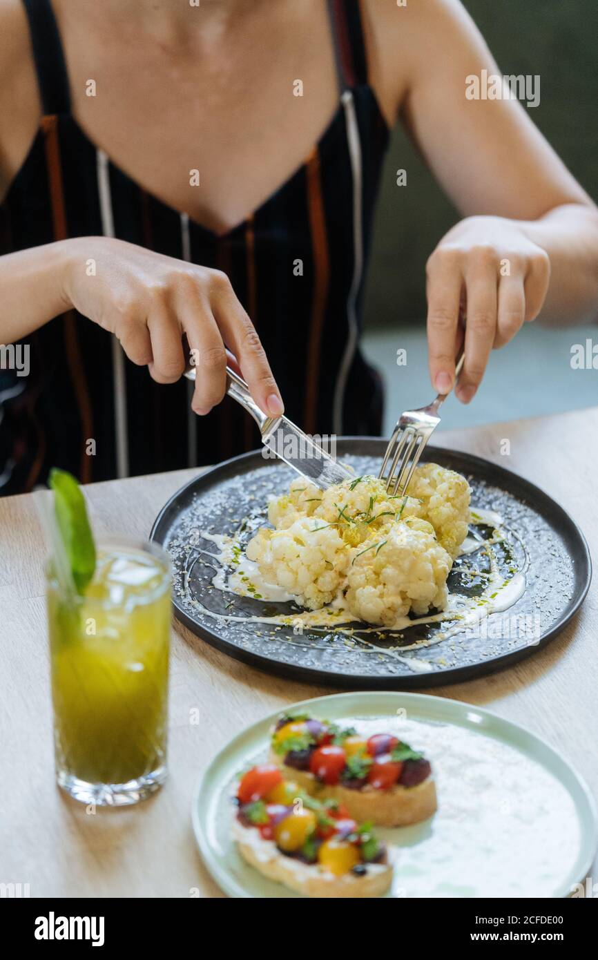 Croise la femme qui coupe le chou-fleur dans la sauce à table avec des sandwiches et de la limonade fraîche au restaurant Banque D'Images