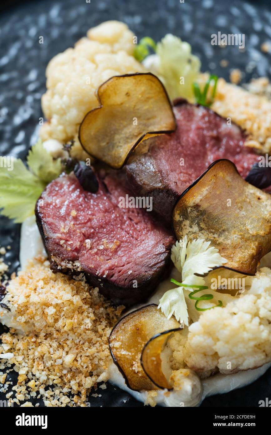 Plaque arrière avec tranches de rôti de bœuf sur une sauce crémeuse avec chou-fleur et frites avec un verre de rouge vin Banque D'Images