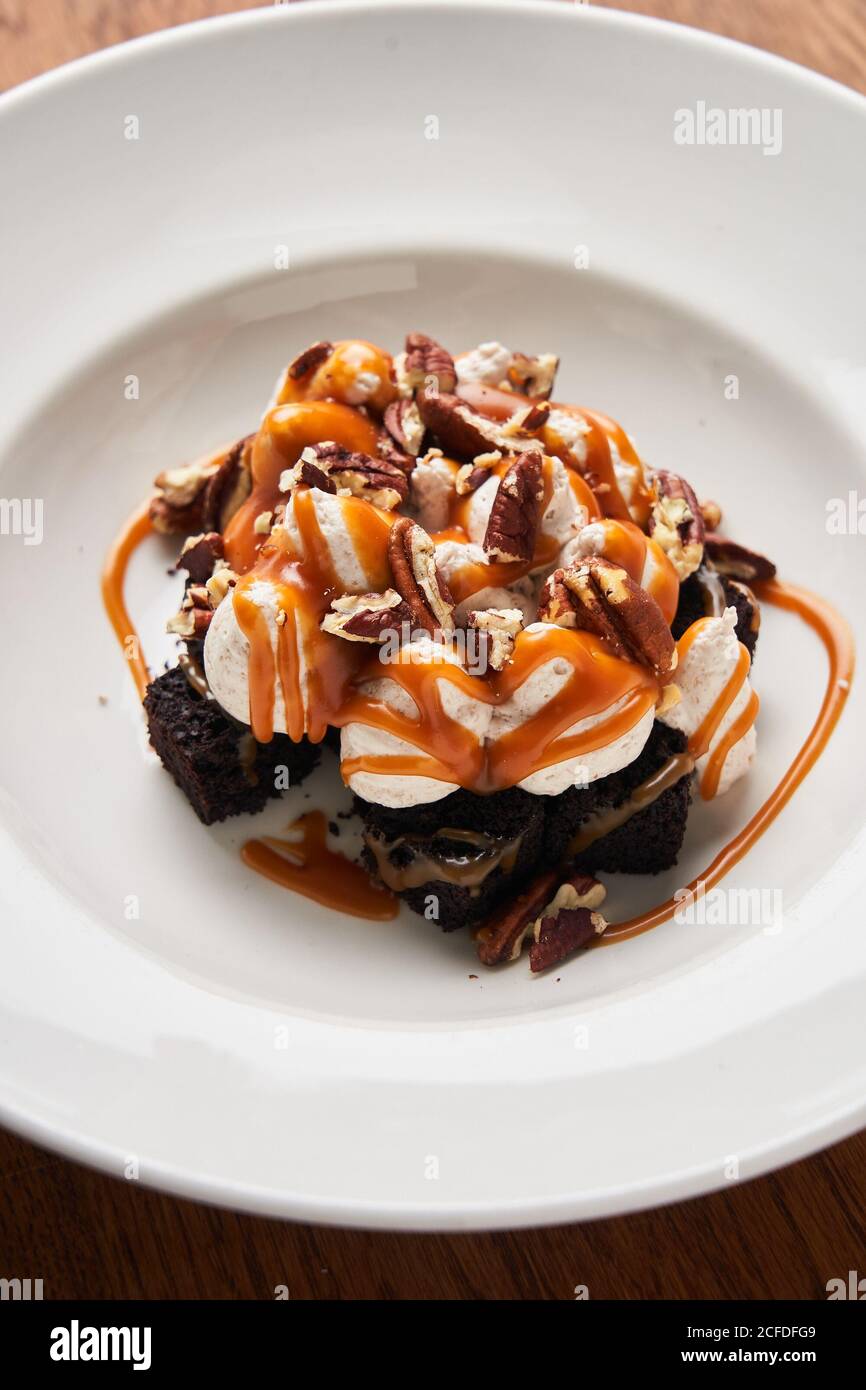 Du dessus des tranches de brownies avec de la crème glacée blanche et des morceaux de chocolat servis avec du caramel sur une assiette blanche Banque D'Images