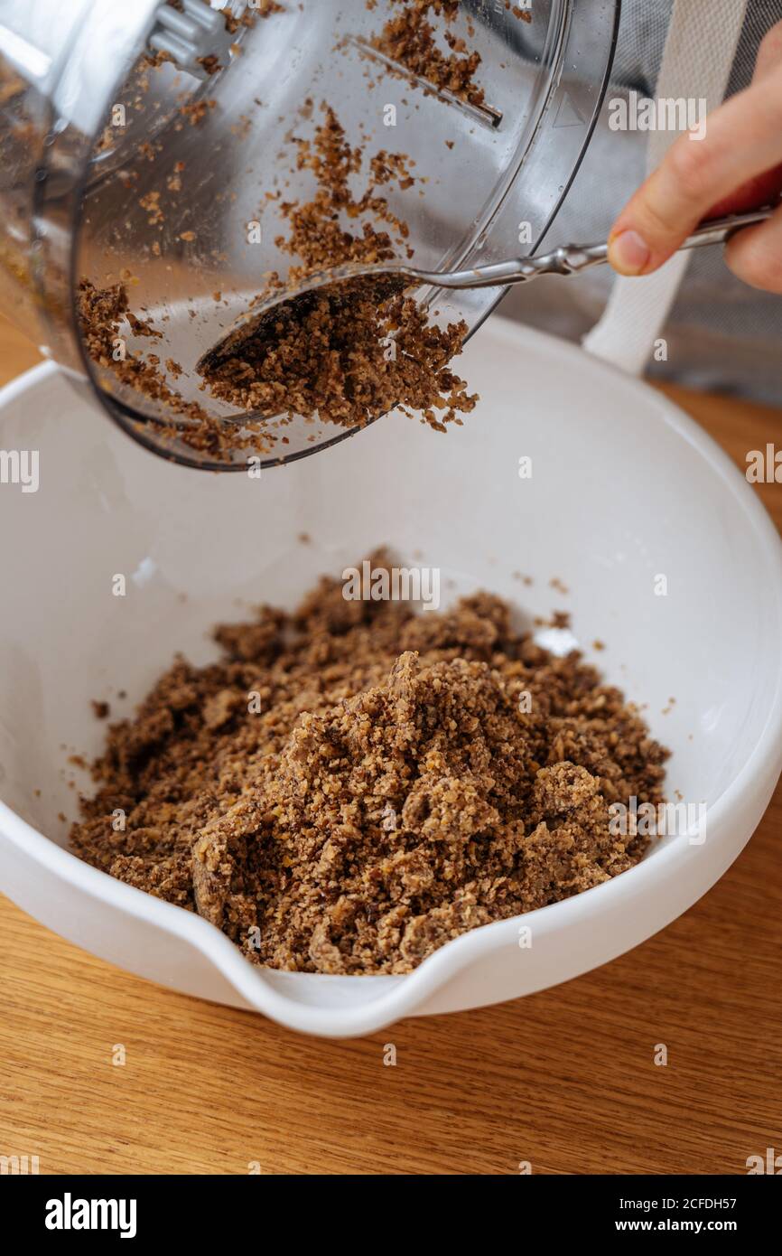 Faites la récolte de la femme au foyer avec une cuillère en mettant les lentilles brunes moulées de la nourriture processeur dans un grand bol blanc placé sur une table en bois Banque D'Images