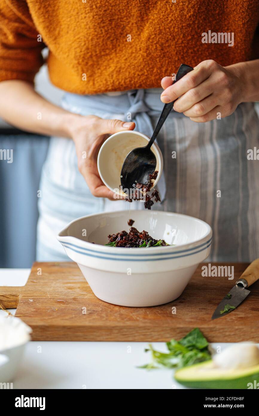 Rognez la femelle en ajoutant des raisins secs noirs dans un bol en céramique blanc placé sur planche à découper en bois tout en préparant la nourriture à la cuisine maison Banque D'Images