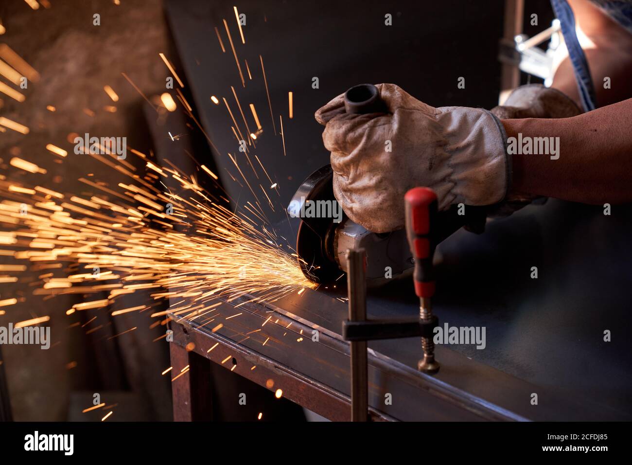 Coupe des mains du travailleur dans des lunettes de protection et des gants métal avec moulin à étincelles volantes pendant les travaux en atelier Banque D'Images