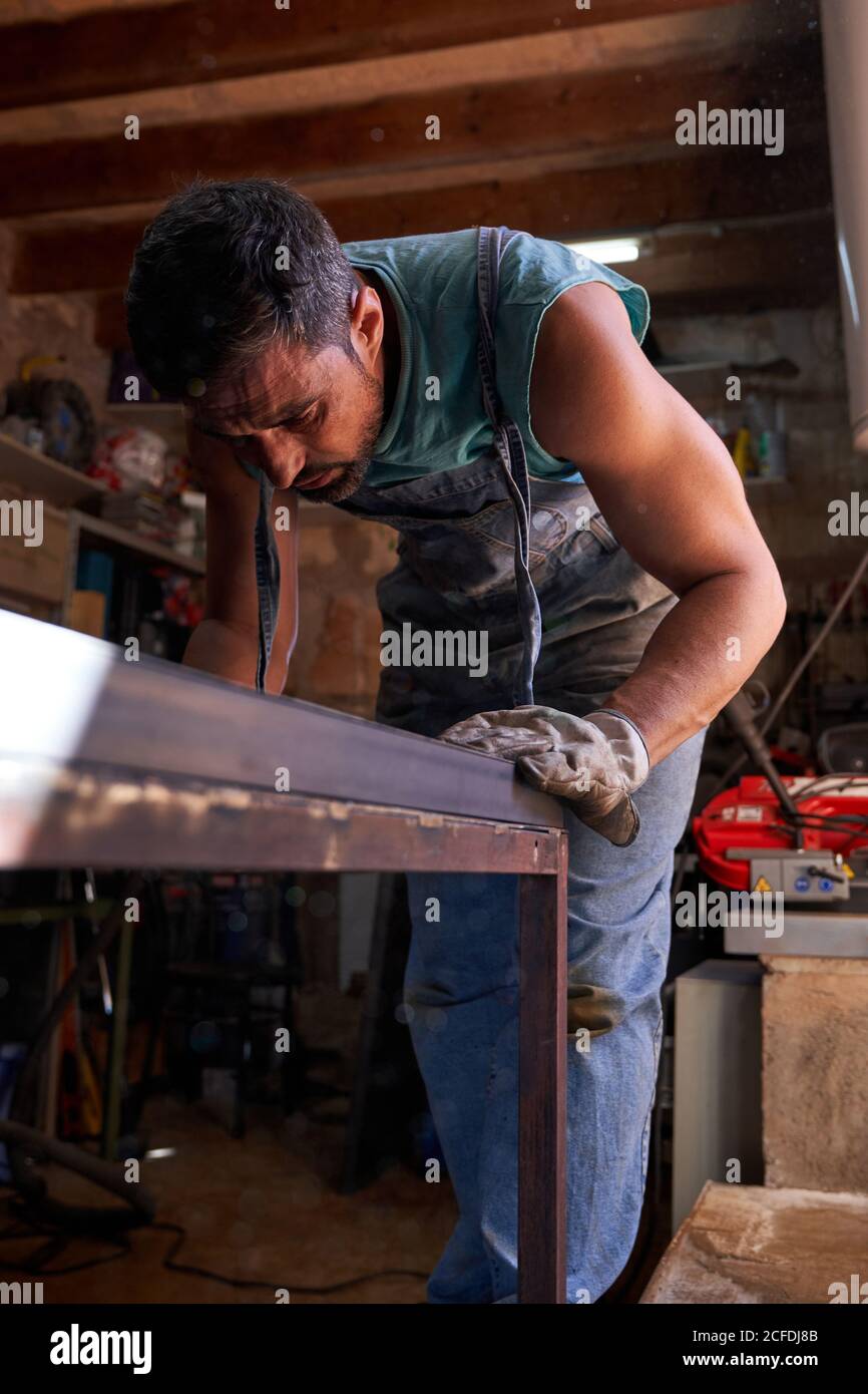 Artisan d'âge moyen en gants de protection marquant la tôle pendant travail en atelier Banque D'Images