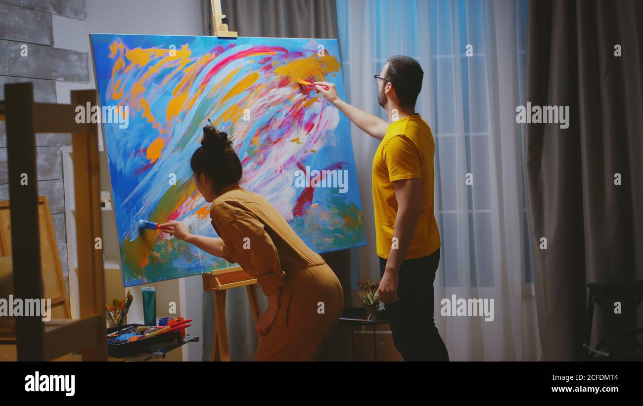 Homme et femme peintres travaillant ensemble dans un studio d'art sur une grande toile. Banque D'Images
